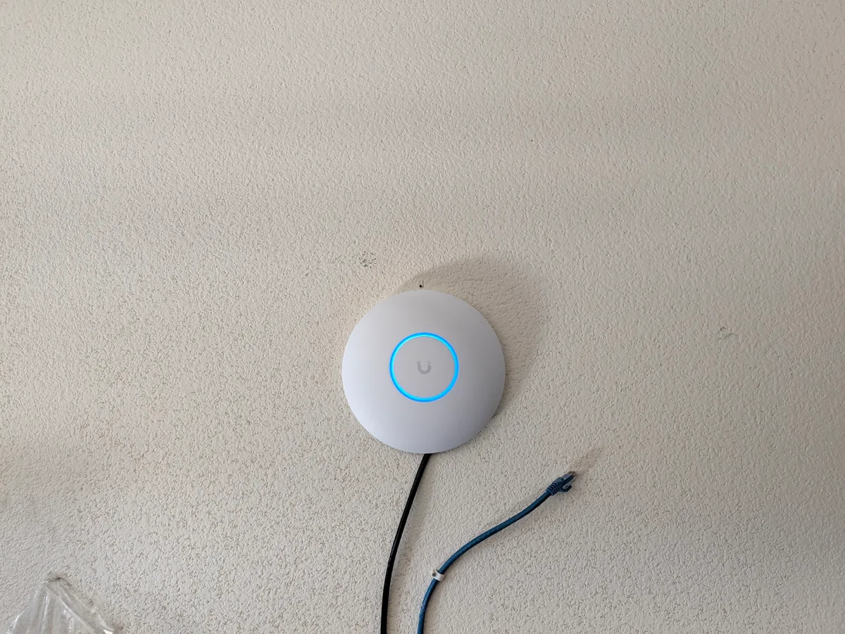 The replacement UniFi U7 Lite mounted on the garage wall, LED ring lit blue after adoption
